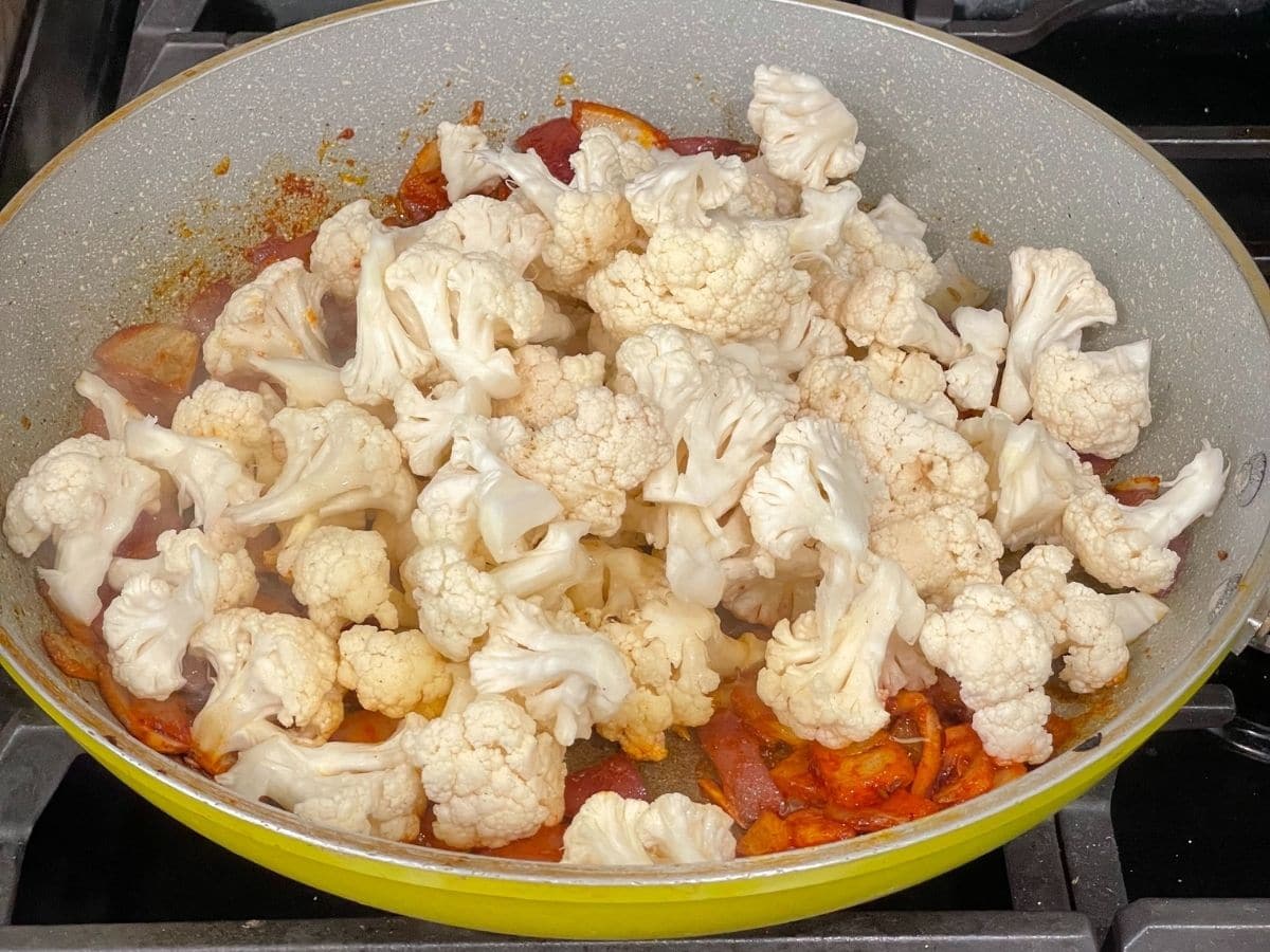 A pan is with spices and cauliflower and its on the heat