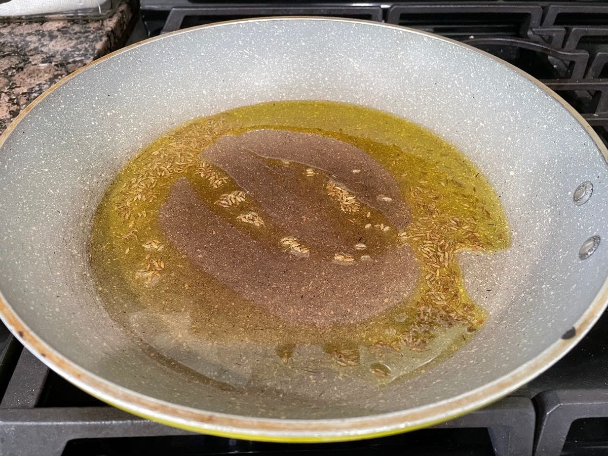 A pan is with oil and cumin seeds over the heat