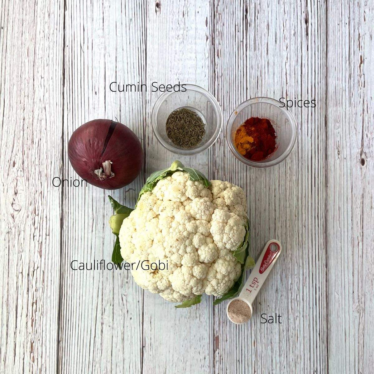 A head of cauliflower, onion, and other ingredients are on the table for sabzi