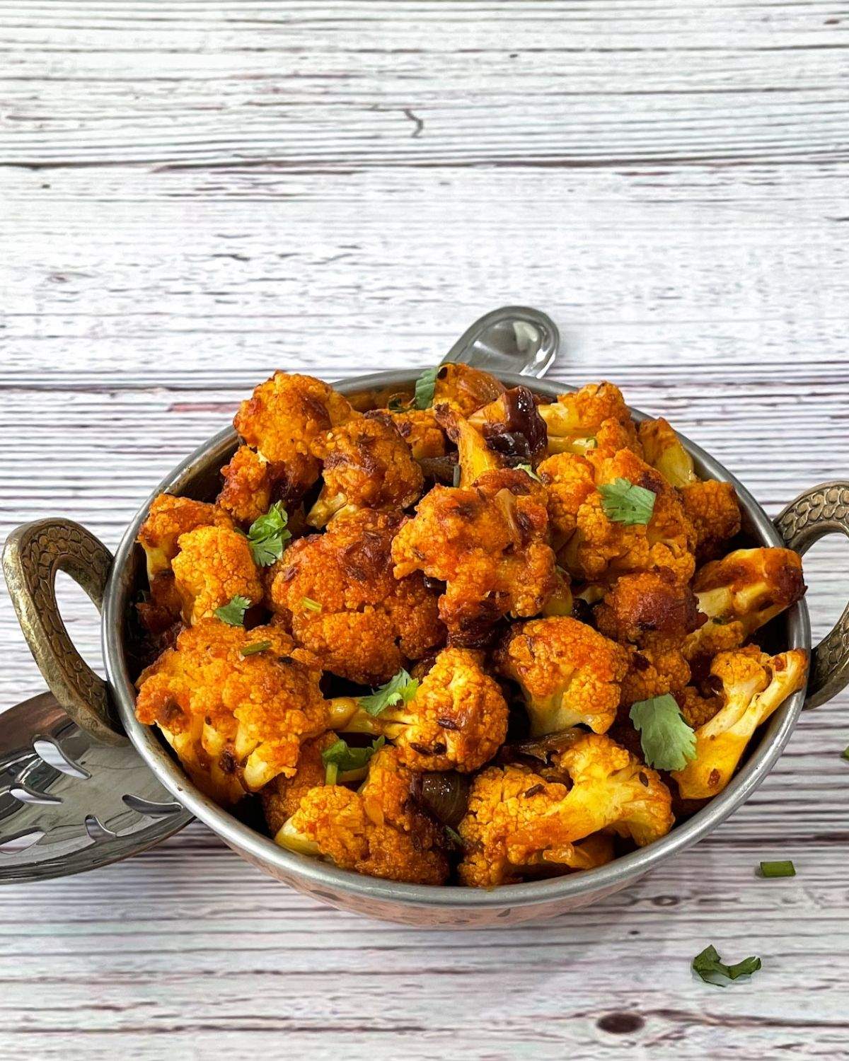 A copper bowl is with gobi sabzi and topped with coriander leaves.