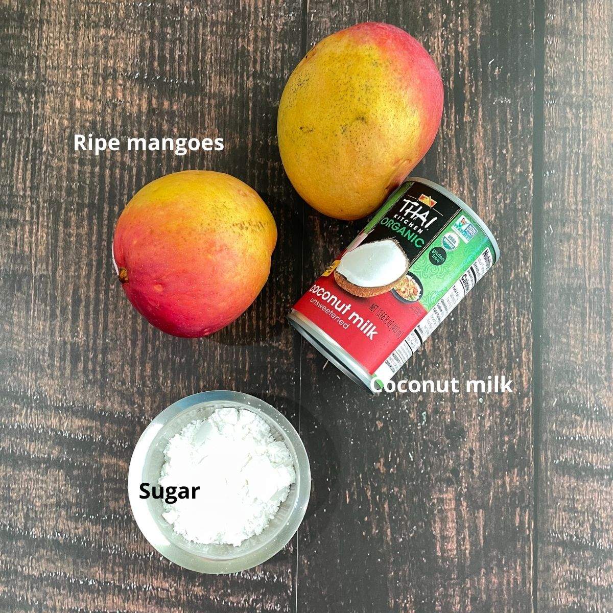 Two ripe mangoes, canned coconut milk, and sugar is placed aon the table for mango ice cream