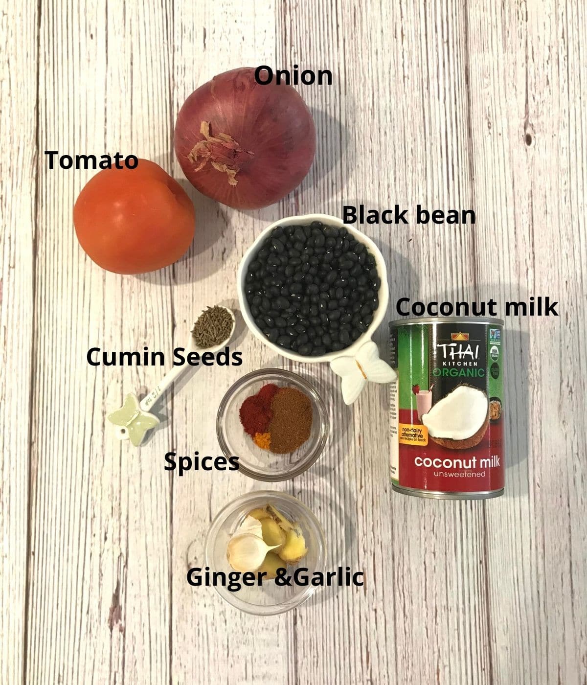 A table is filled with black bean, tomatoes, onion, spices for black bean curry