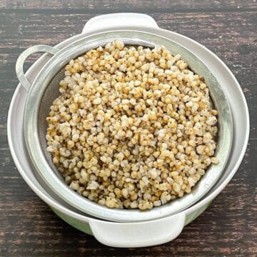 A strainer is filled with cooked sorghum on the table