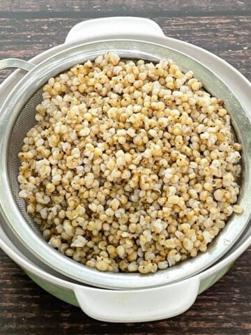 A strainer is filled with cooked sorghum on the table