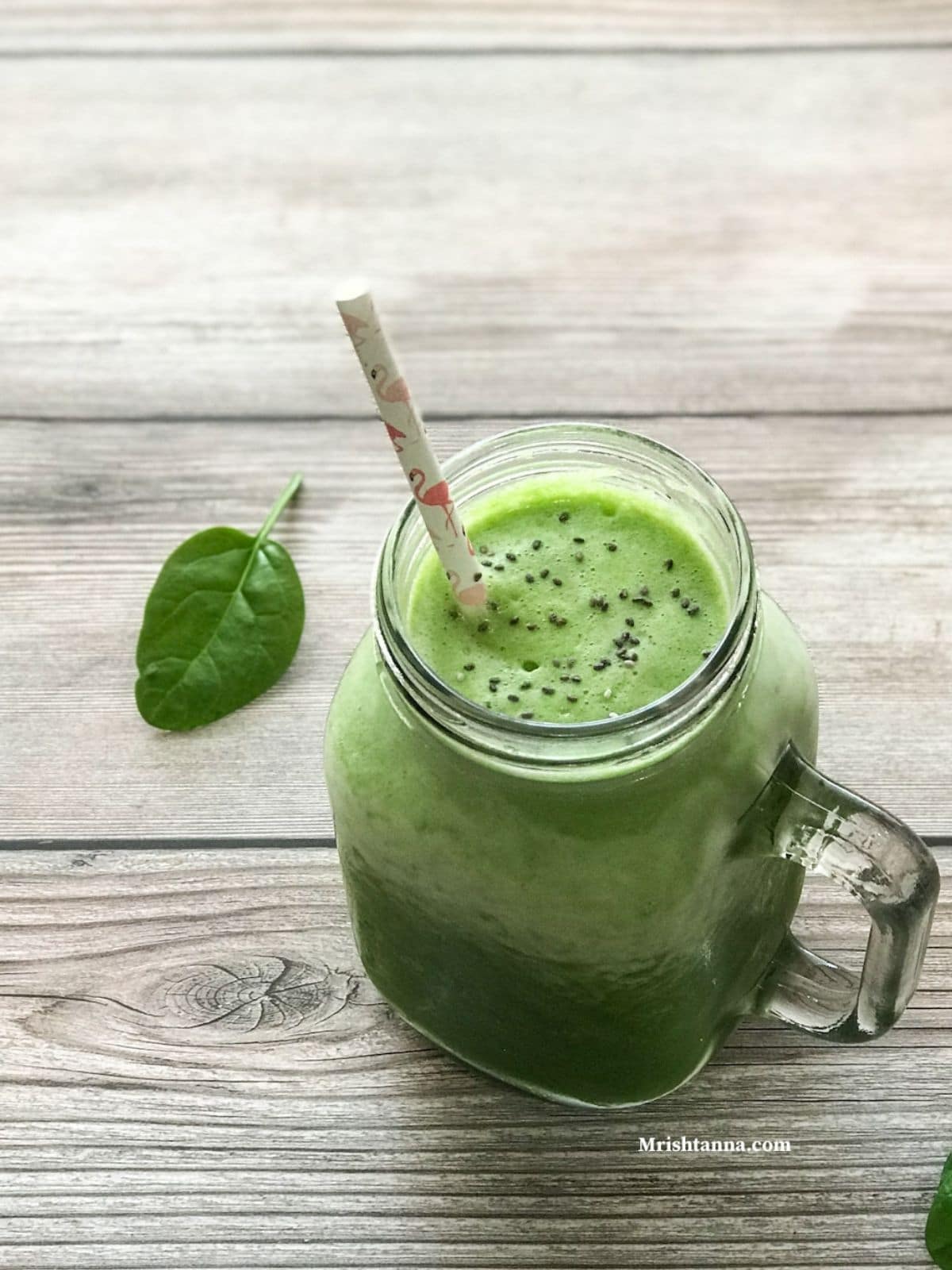 A glass is full of Pineapple green smoothie and topped with chia seeds and its on the table