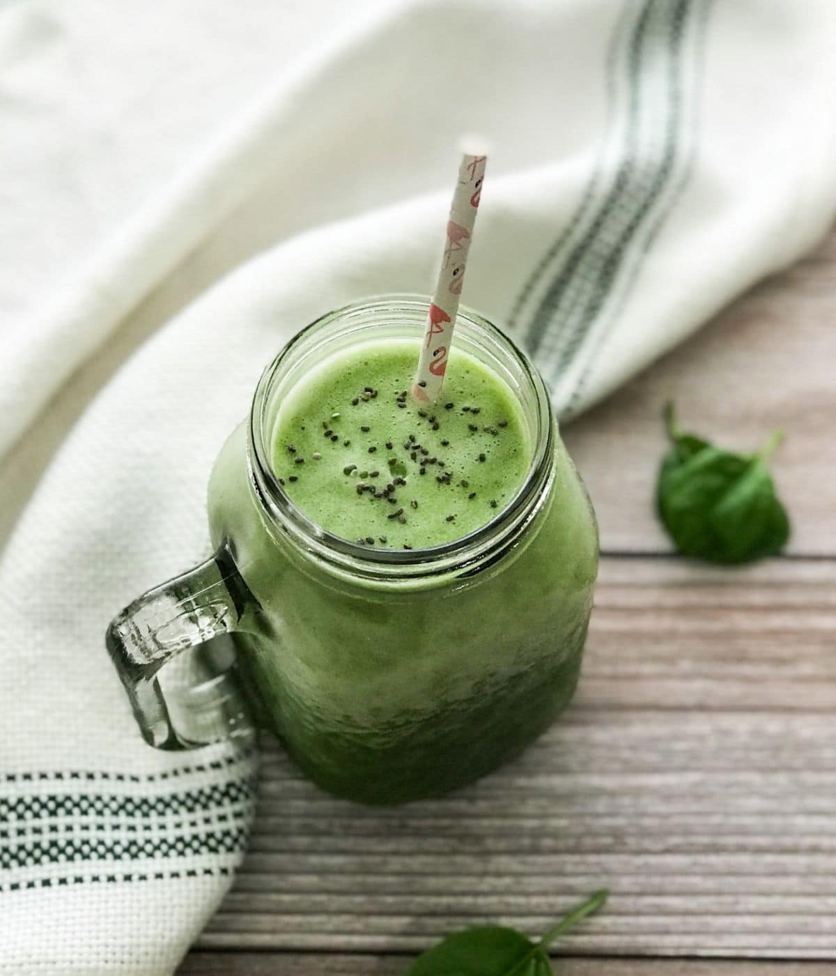 A glass of pineapple spinach smoothie is on the table with a straw 