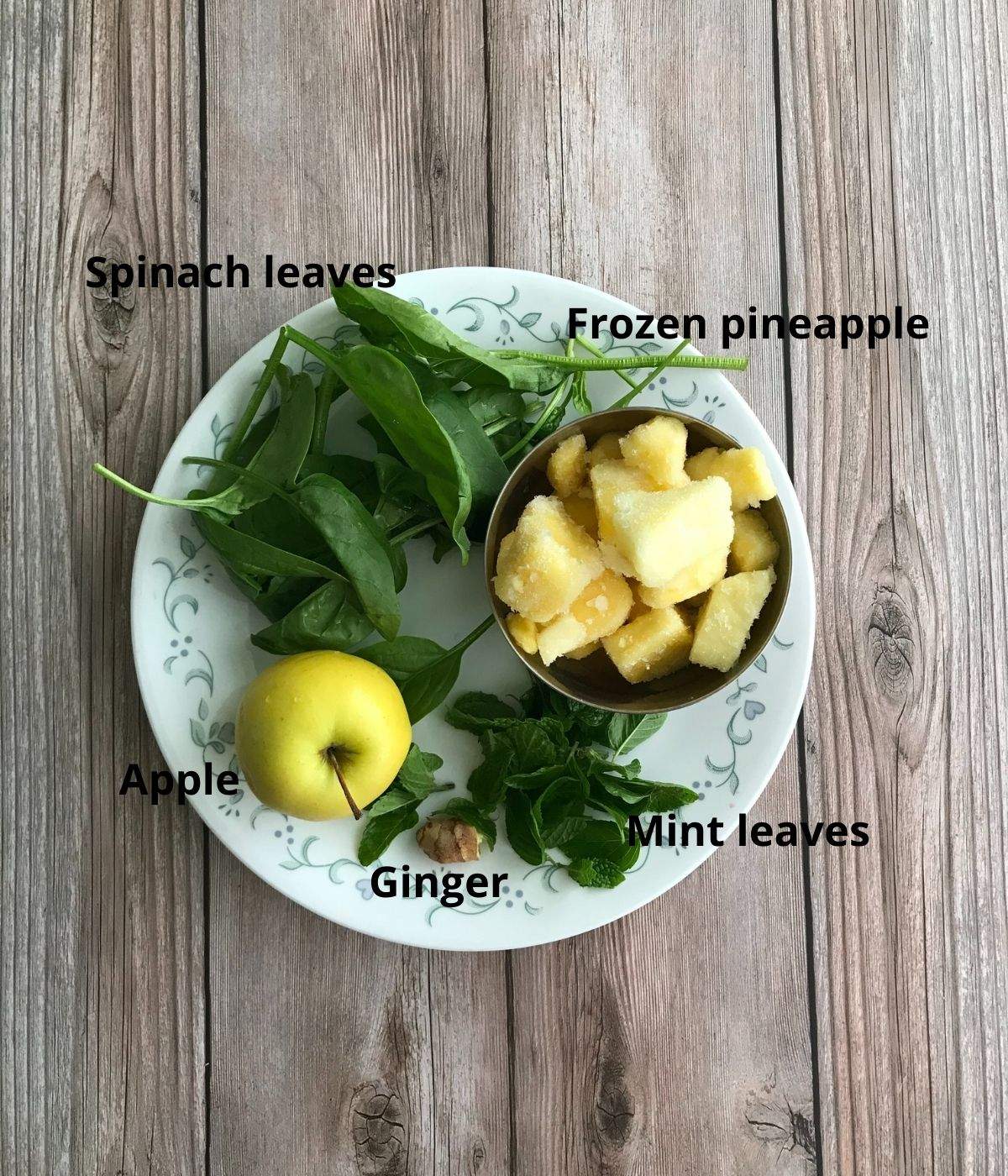 A plate is with spinach, apple, pineapple for spinach smoothie