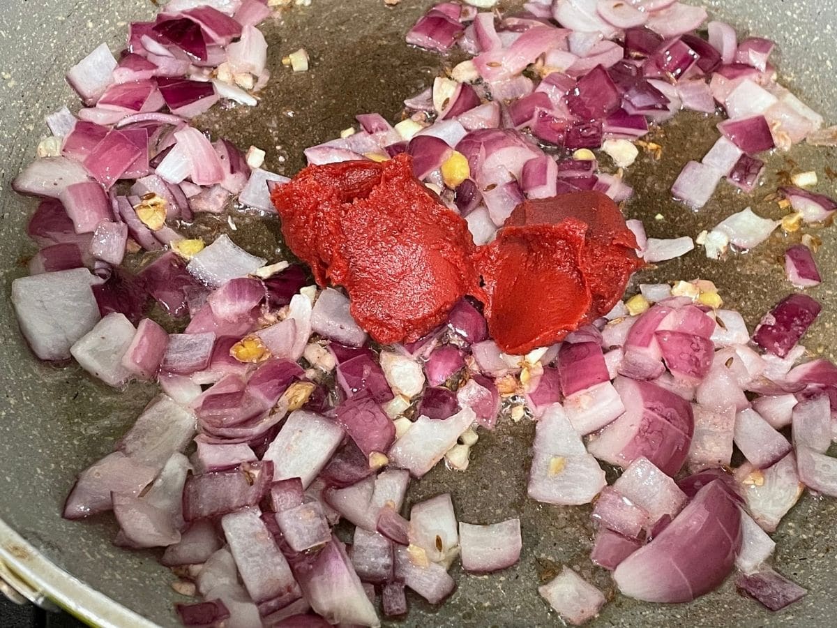 A pan is with onions, and tomato paste over the heat