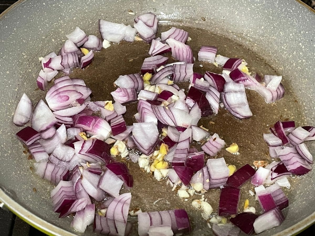 A pan is with oil, cumin seeds, and onions over the heat.