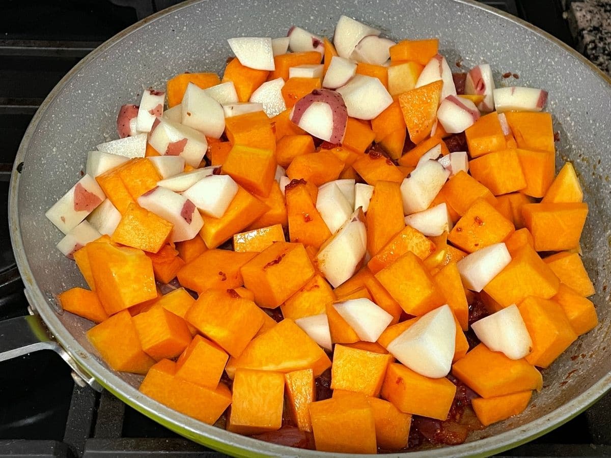 A pan is filled with cubed potatoes and pumpkins over the heat.