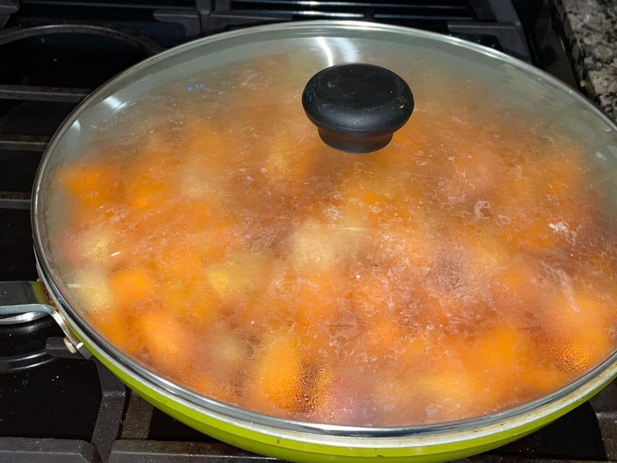 A pan is filled with veggies and covered with lid and placed over the heat