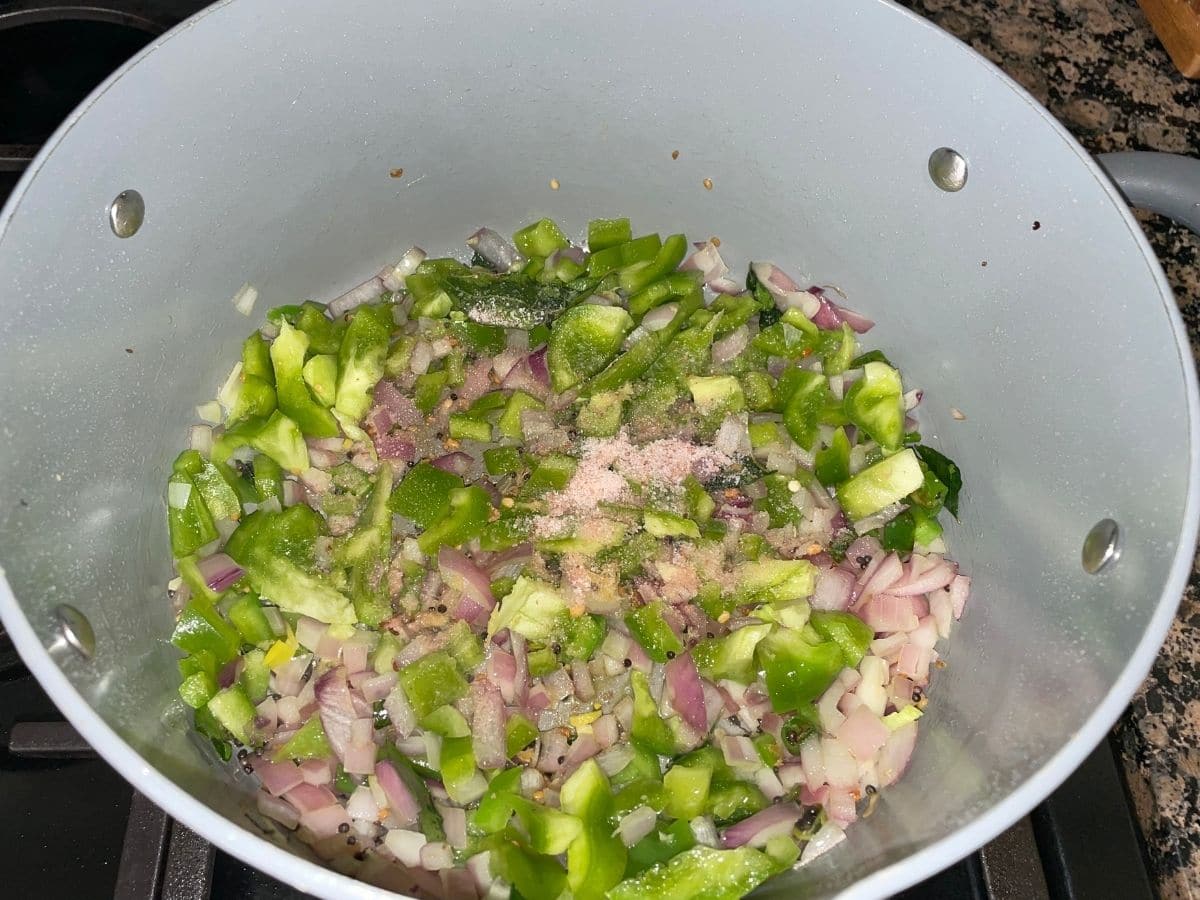 A pot is placed on the heat and filled with onions and bell pepper