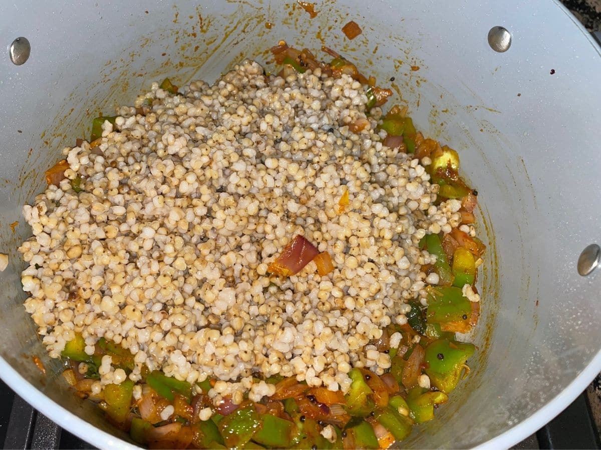 A vessel is with cooked sorghum and vegetables over the stove top