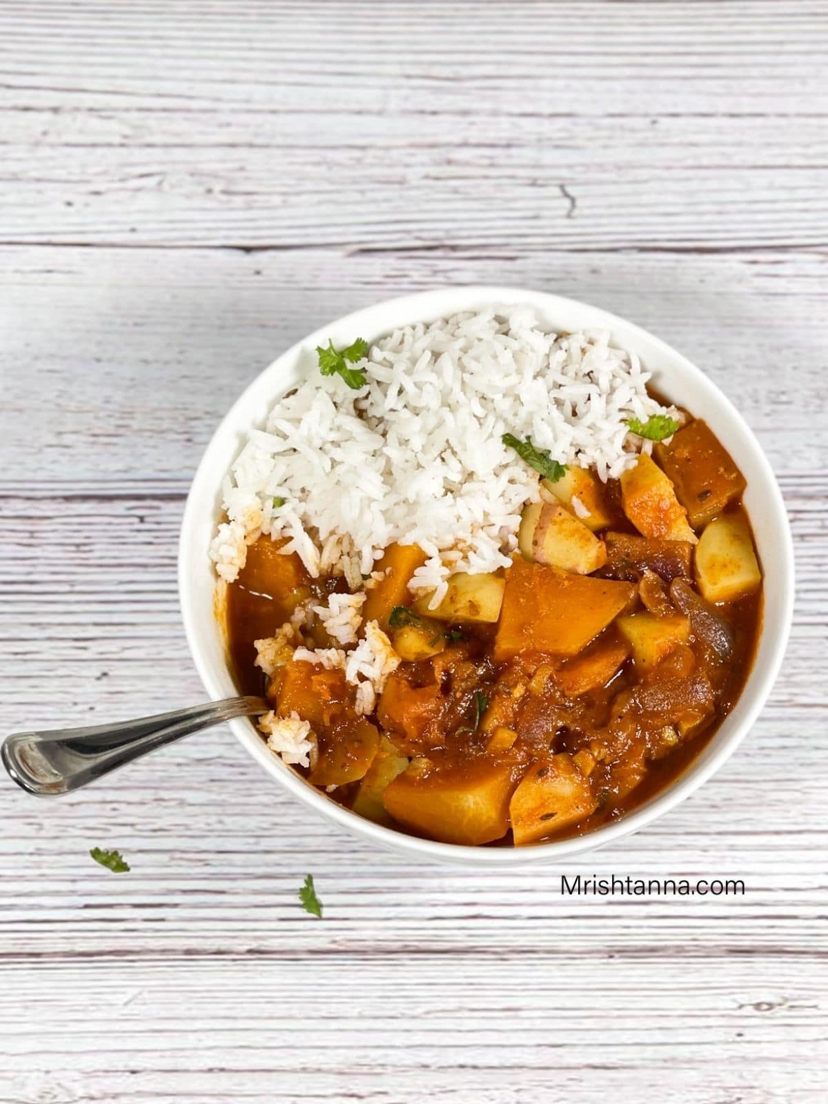 A bowl is with pumkin curry and rice with a spoon inside place on the table.