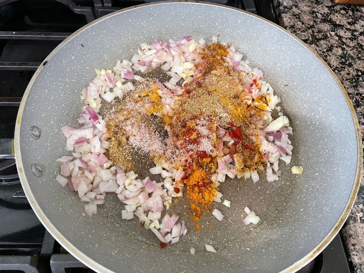 A pan is with onions and spices over the heat.