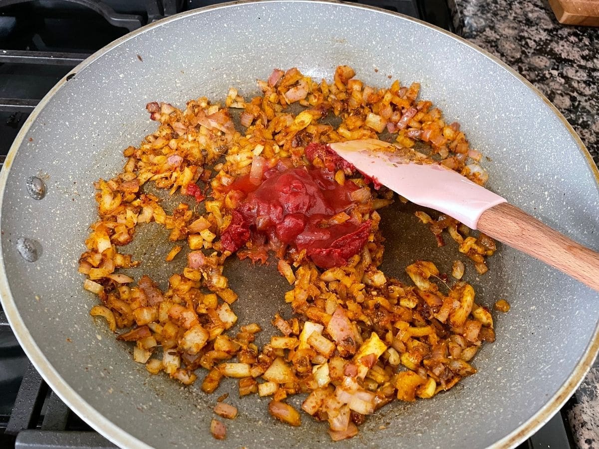 A pan is filled with onions, spices and tomato paste for curry