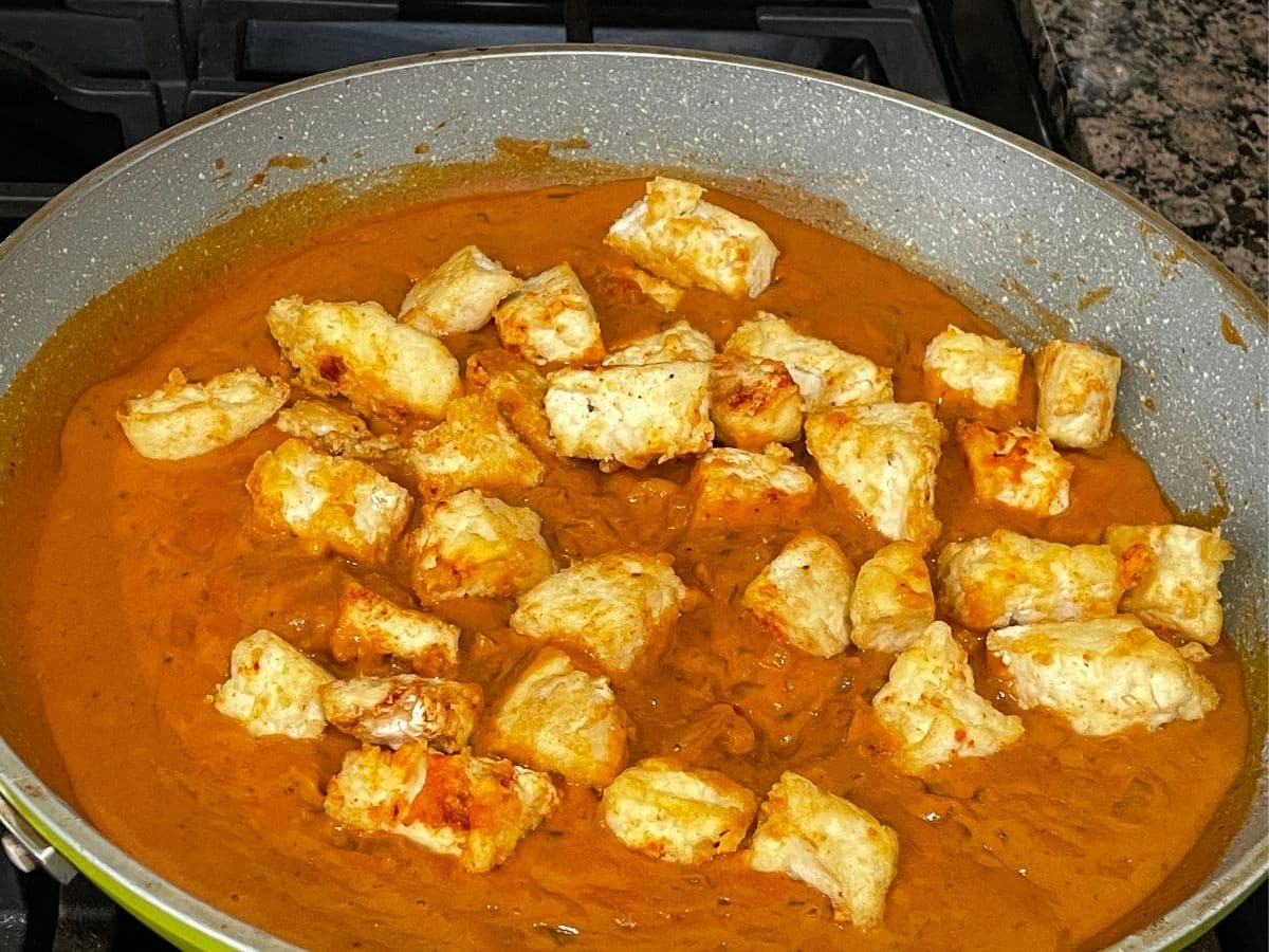 A pan is filled with vegan butter chicken curry over the heat