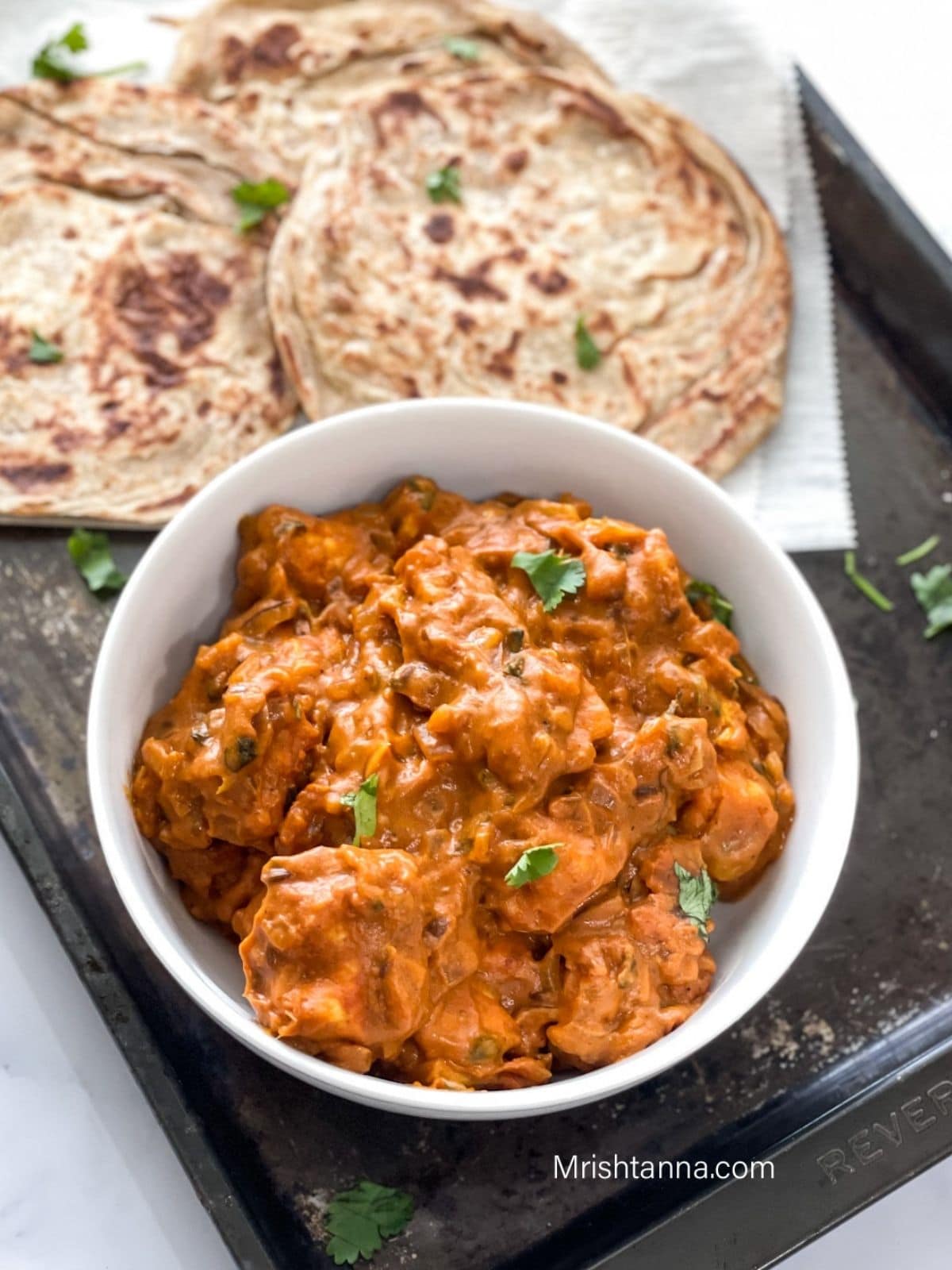 A white bowl of vegan butter chicken curry is on the black tray.