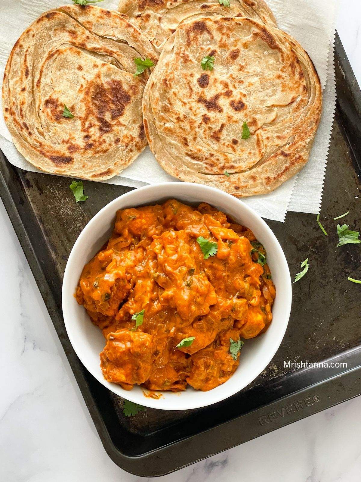 A bowl is filled with tofu butter chicken curry and placed on the baking tray along with paratha.