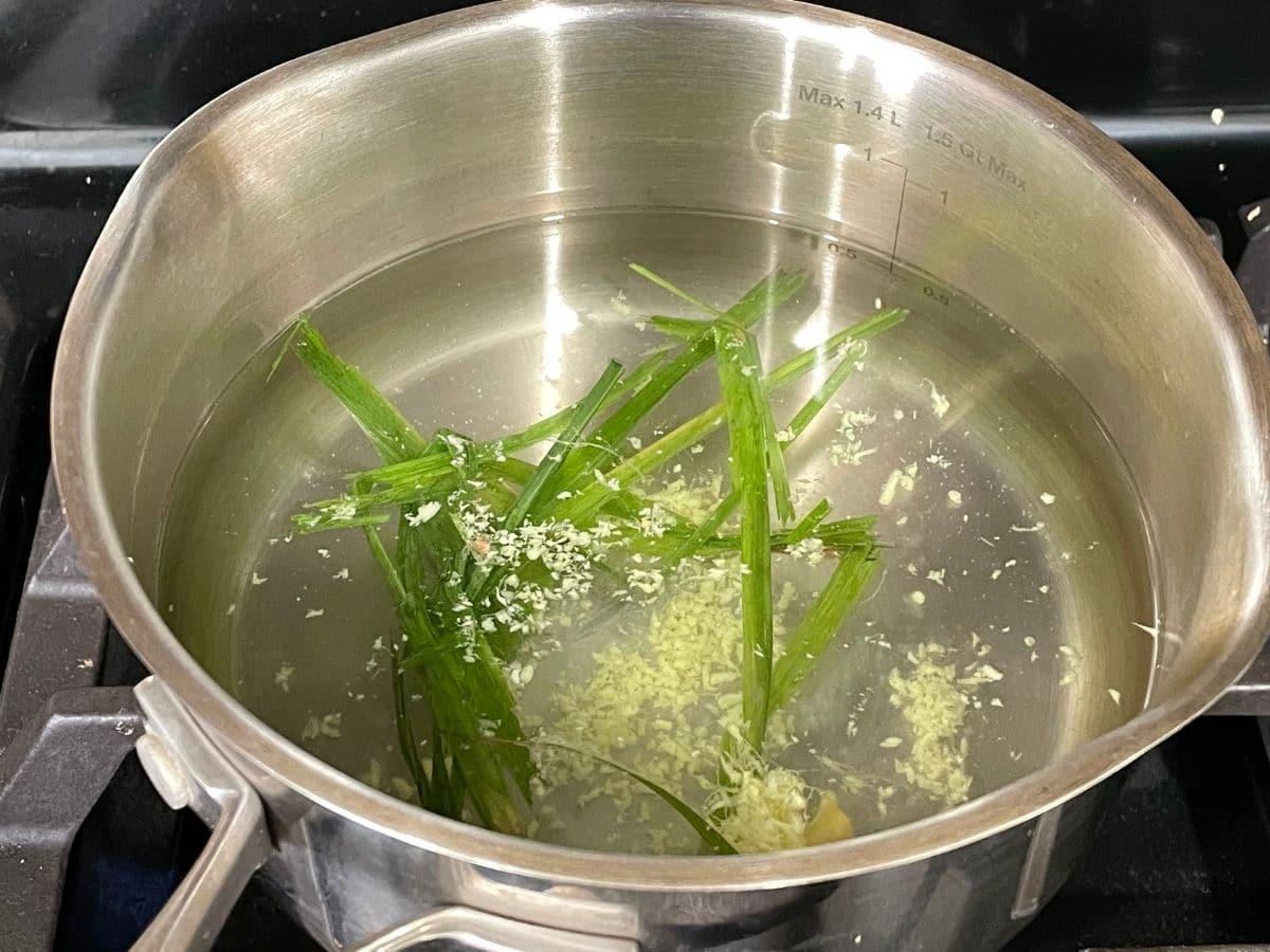A small pot is with water, lemongrass, and ginger over the heat.