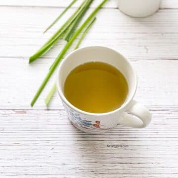 A white cup is filled with lemongrass tea and is on the table