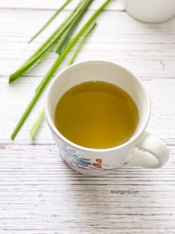 A white cup is filled with lemongrass tea and is on the table