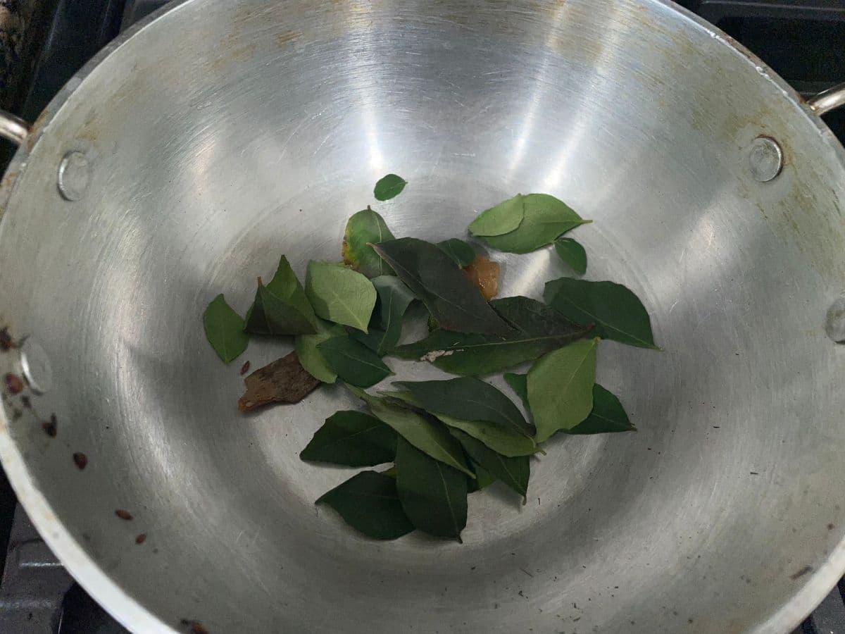 A pan is with curry leaves and spices over the medium heat