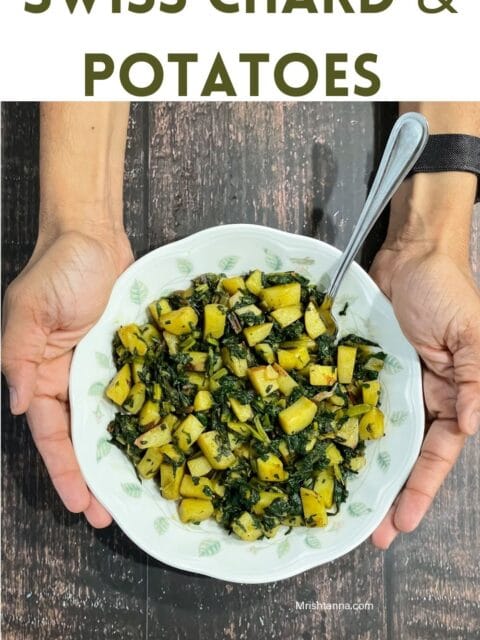 A man is holding up a plate which is filled with Swiss chard and potato fry.