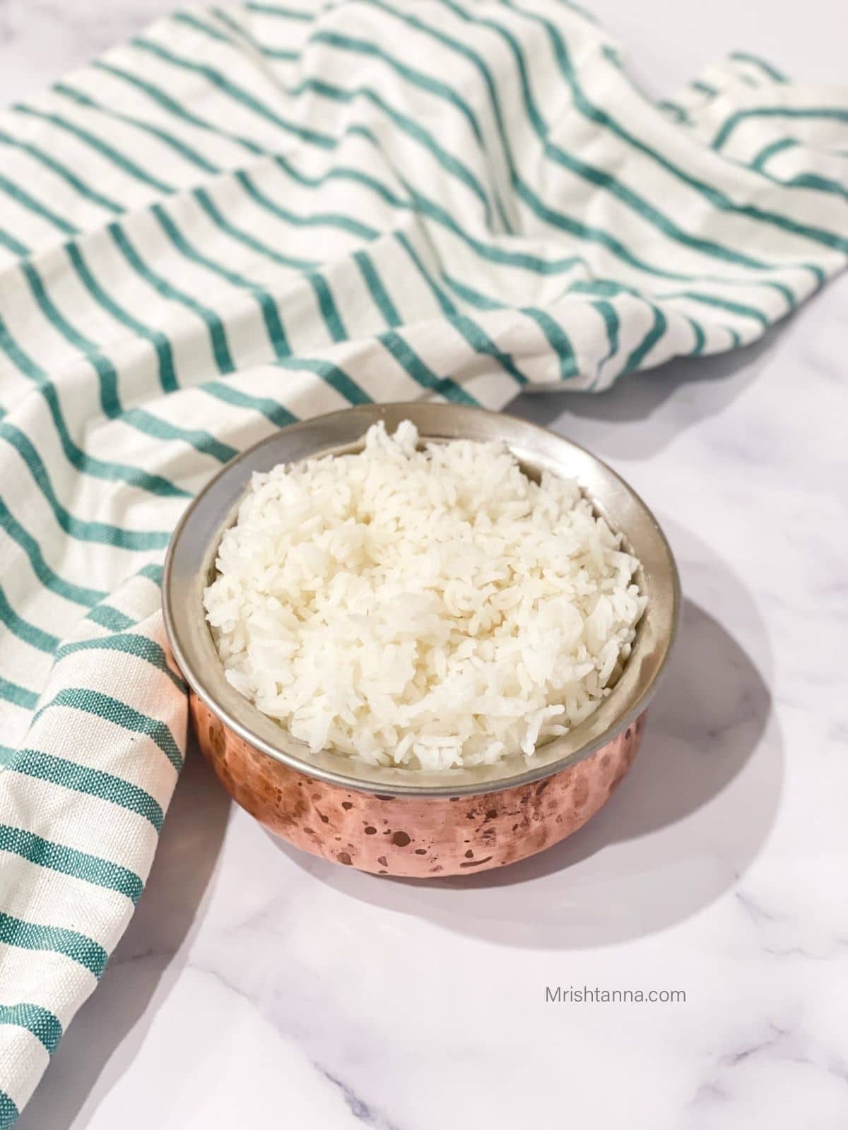 A copper pot is with cooked sona masoori rice on the table.