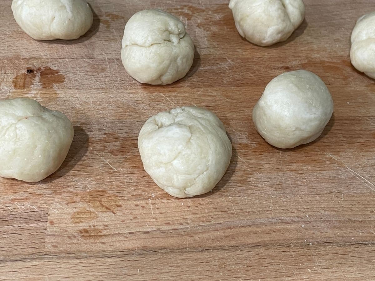 Small round shaped dough is on the wooden board.