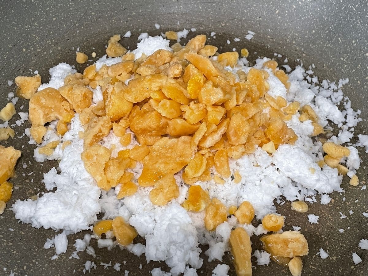 A pan is filled with coconuts and jaggery over the heat.