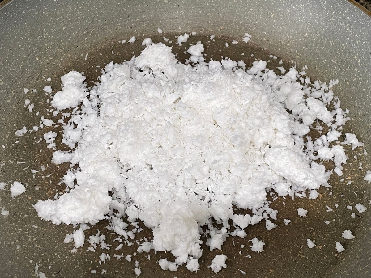 A pan is with grated coconuts over the heat for karjikai stuffing.