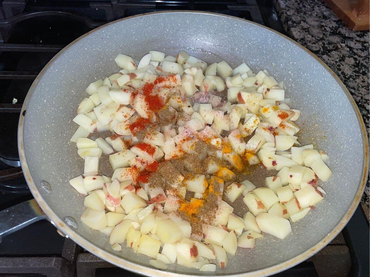 A pan is with potatoes and spices over the heat