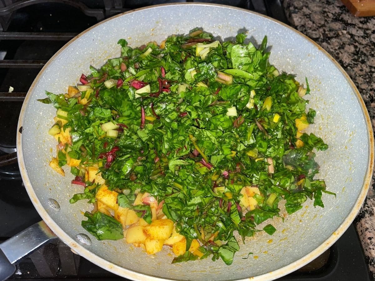 A pan is with cooked potatoes and chopped Swiss chard over the heat