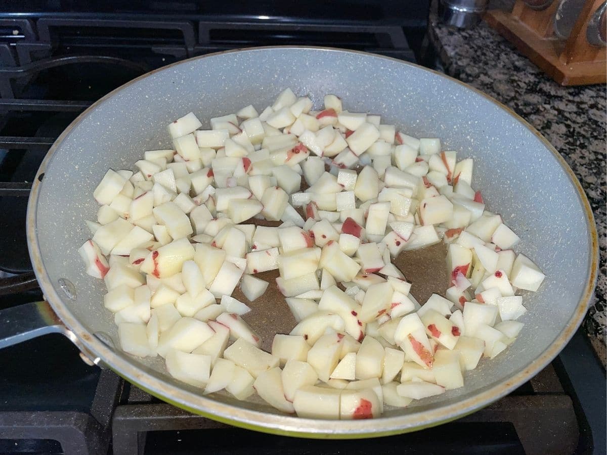 A non stick pan is with cubed potatoes over the heat.
