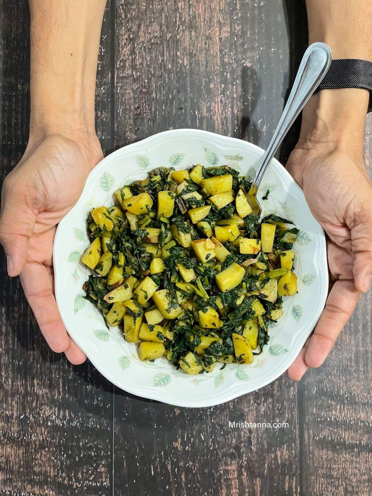 A man is holding up the plate with swiss chard and potatoes