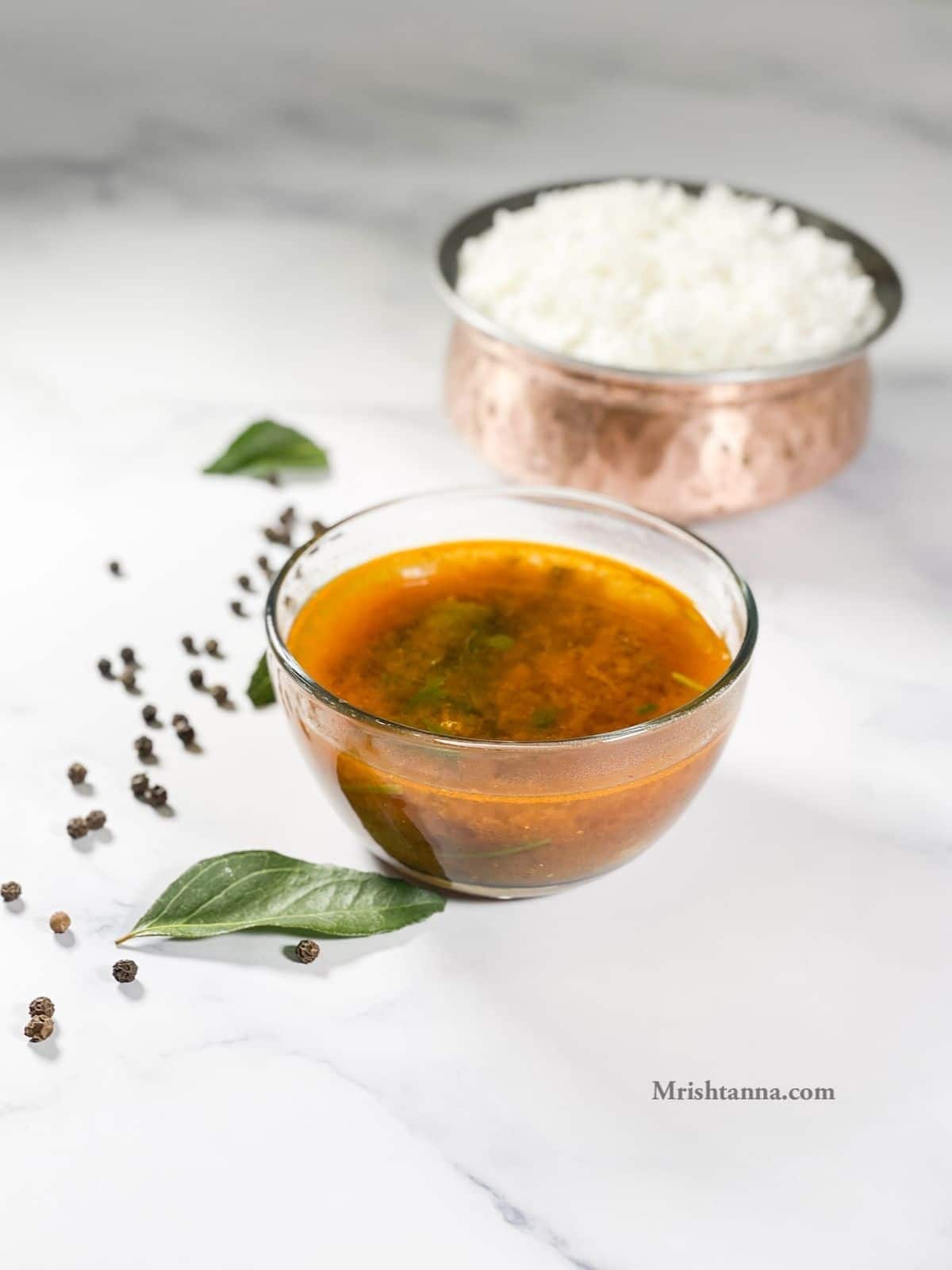 A glass bowl is with pepper rasam on the table