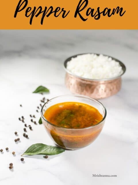 A glass bowl of pepper rasam is on the white table