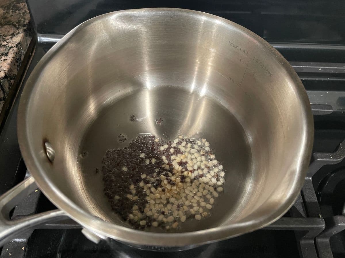 A medium size vessel is with oil and spices over the stove top.