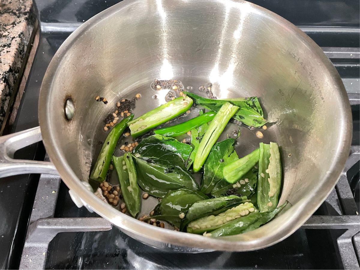 A vessel is with curry leaves and chilies for pepper rasam