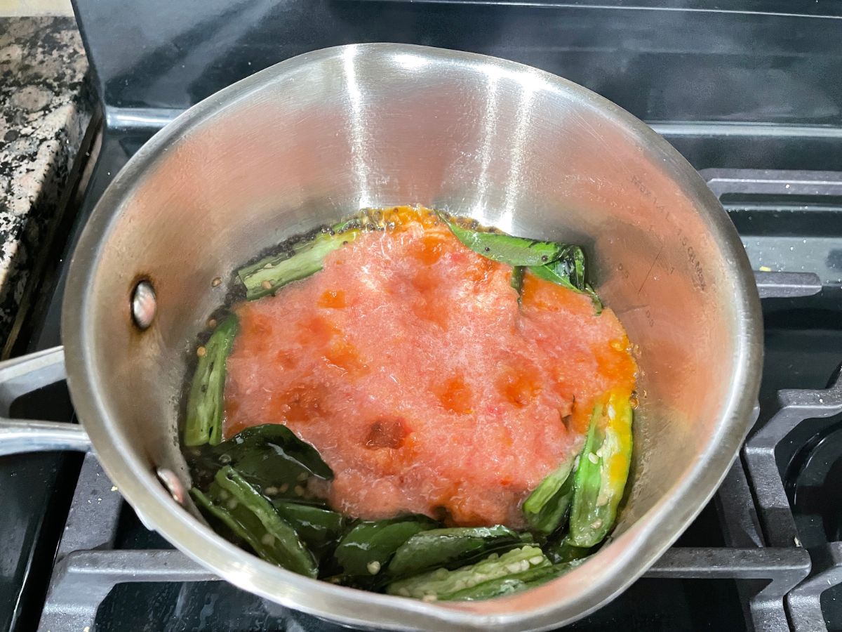 A vessel is with tomatoes and chilies over the heat, with rasam