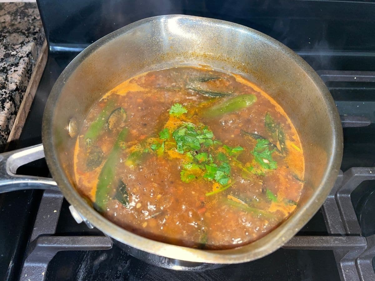 A pot is with pepper rasam and topped with cilantro.