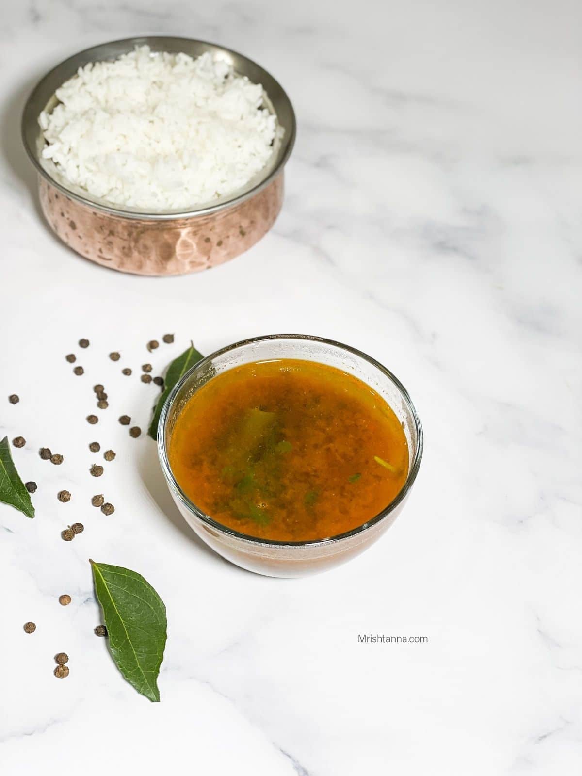 A bowl of pepper rasam is on the table along with sona masoori rice