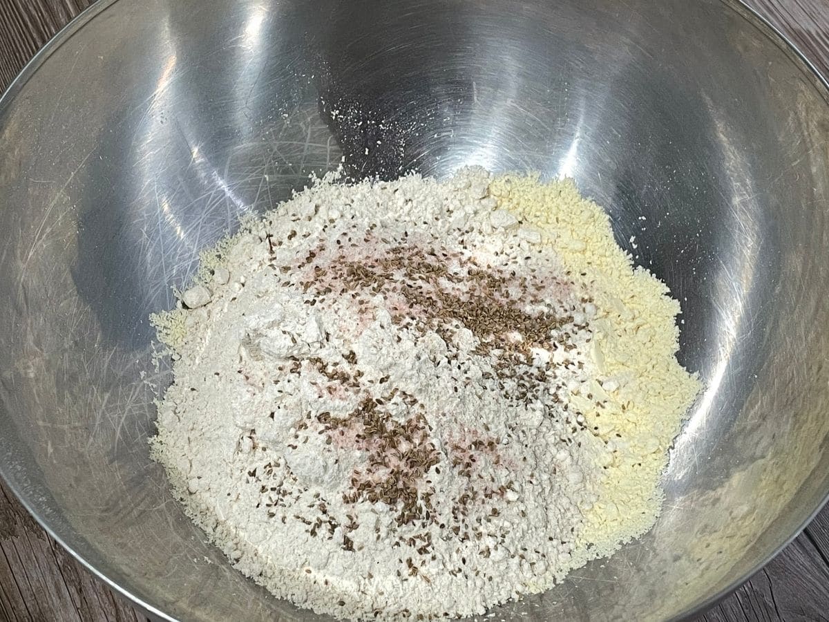 a bowl is filled with flour, ajwain seeds, and salt for roti recipe.