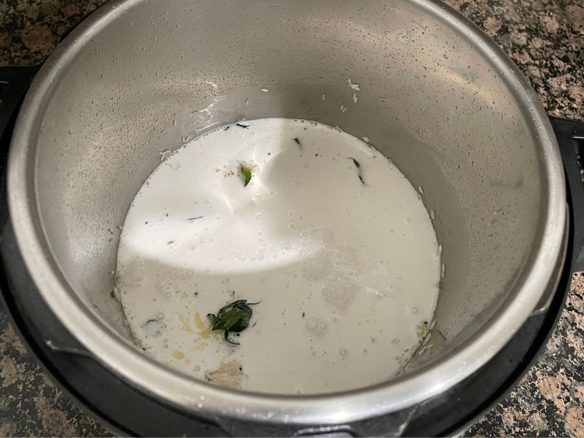 An instant pot is with rice, spices and coconut milk to make coconut rice.
