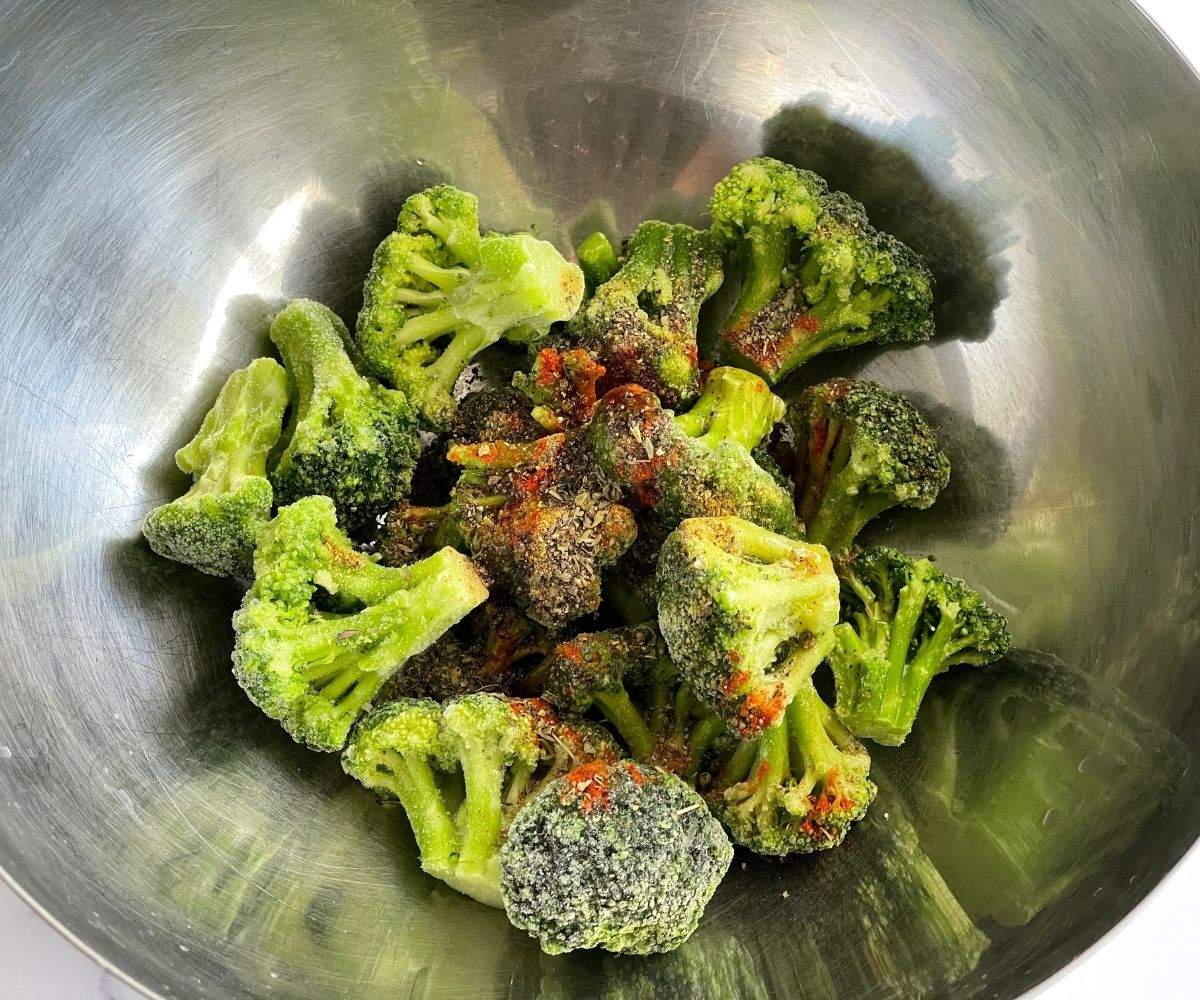 A bowl is with frozen broccoli and seasonings.