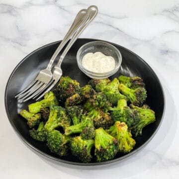 A plate is with air fried frozen broccoli and fork.