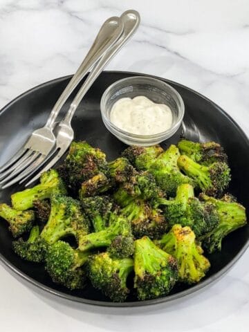 A plate is with air fried frozen broccoli and fork.