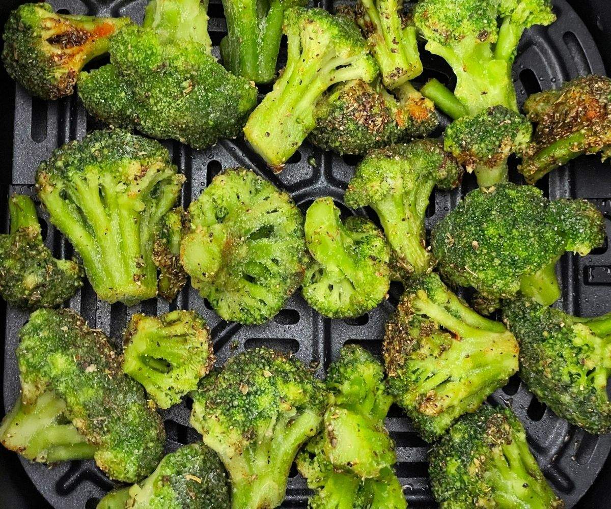 frozen broccoli with seasoning placed inside the air fryer basket.