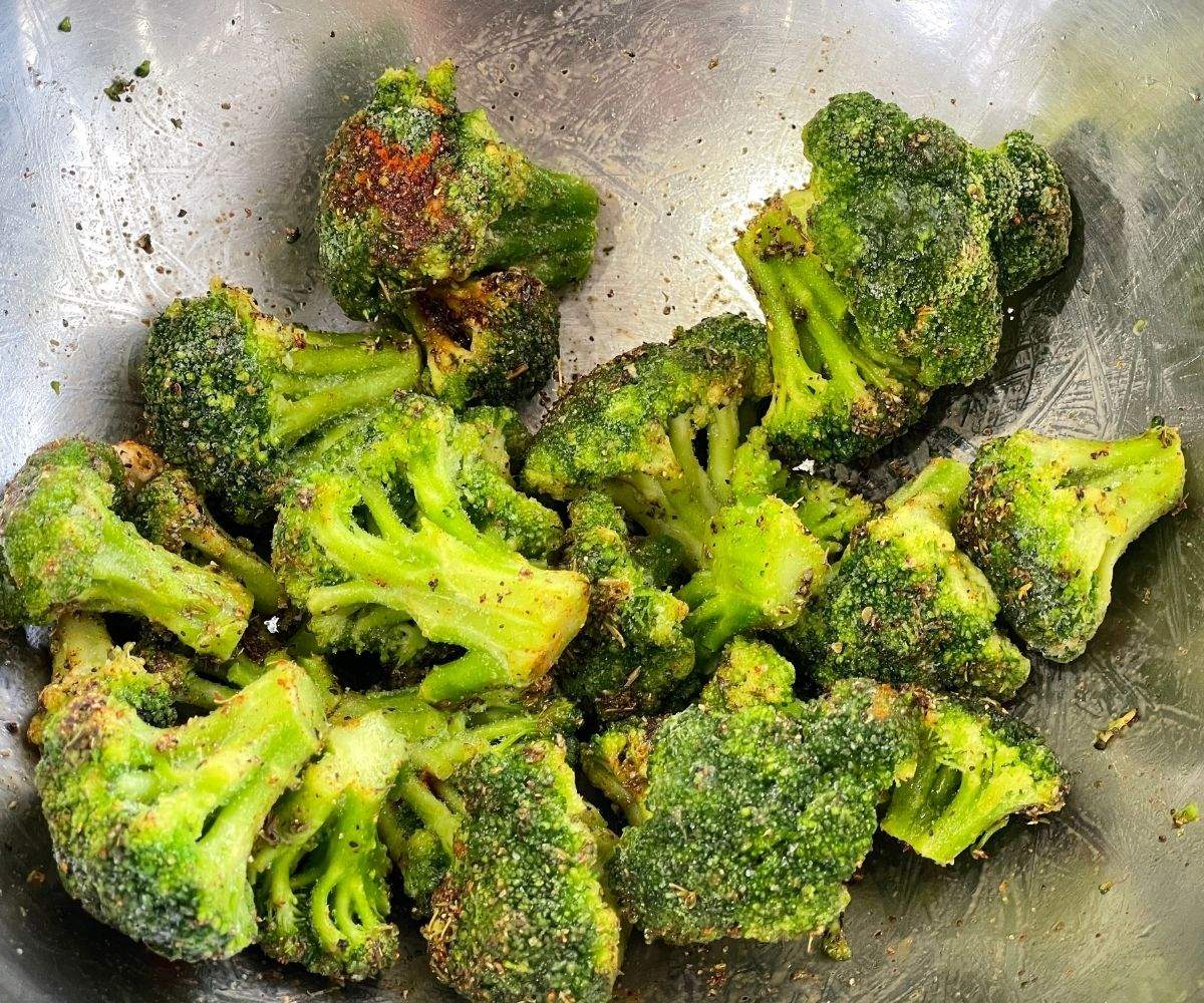 Frozen broccoli is mixed with seasonings inside the bowl.